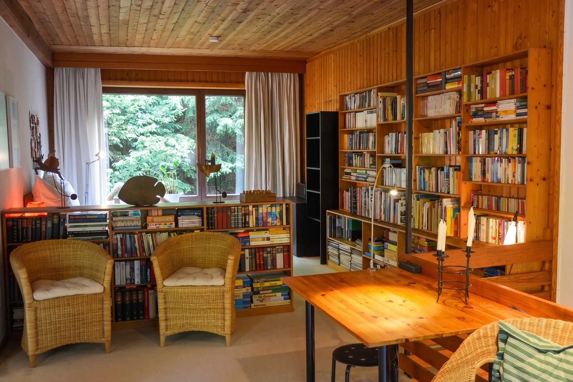 Living room of the holiday flat with library, wicker chairs and a large window onto the trees
