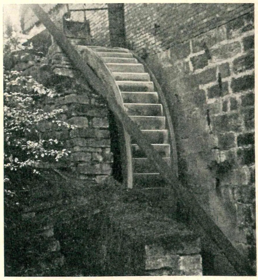 Historic photo of a large water wheel against a rubble-stone wall